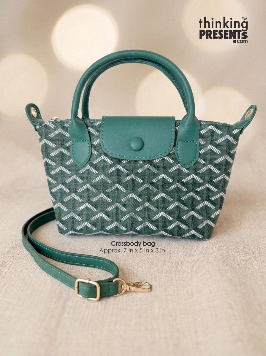 A small crossbody handbag with a teal and white chevron pattern, featuring a top handle, a matching flap closure, and an adjustable shoulder strap with gold-tone hardware. The bag is displayed on a textured beige fabric surface with a warm bokeh background.