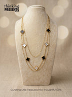 Layered gold-tone necklace with black and white clover accents displayed on a neutral jewelry bust, part of the Black Clover Muse Gift Set by Thinking Presents™