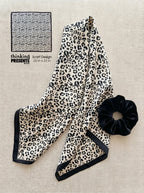 Leopard print scarf and black scrunchie on a beige surface with 'thinking presents' branding.