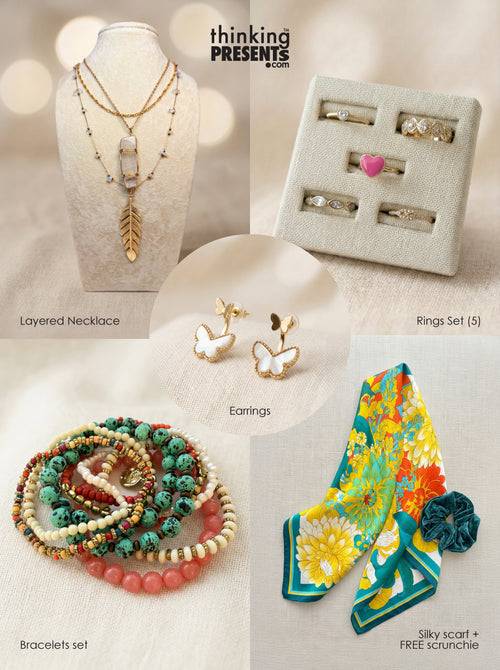 Curated gift set featuring layered gold-tone necklace with clear stone pendant and feather charm, butterfly earrings, five-piece ring set with heart detail, colorful beaded bracelets, and a vibrant floral silky scarf with matching scrunchie, styled as a bold and feminine ready-to-gift set