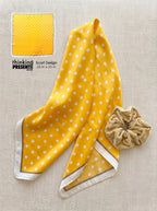 Yellow polka dot scarf with a beige scrunchie on a beige background