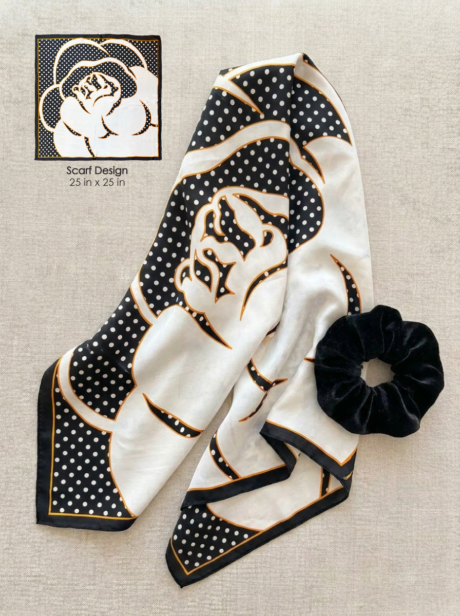 A folded scarf with a cream and black floral design, black polka dot patterned corners, and gold trim, displayed on a beige textured fabric background next to a black scrunchie. A small graphic in the top left shows the scarf design details with text reading 'Scarf Design 23 in x 23 in'.