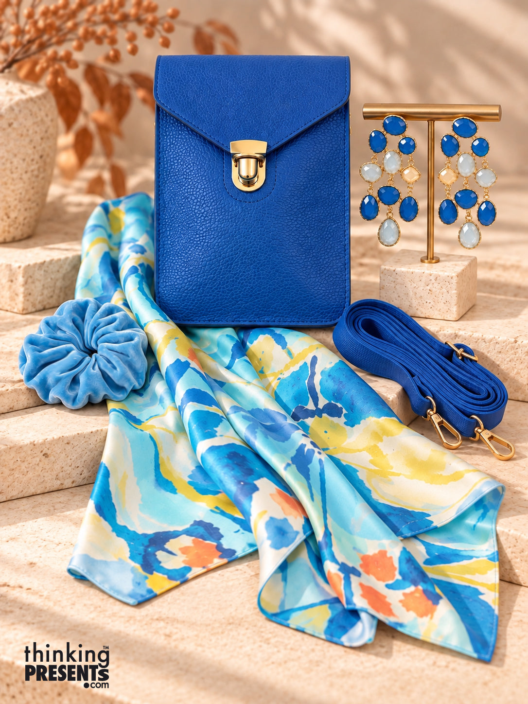 Cobalt blue vegan crossbody bag with gold push lock, chandelier earrings, silky watercolor scarf, and velvet scrunchie