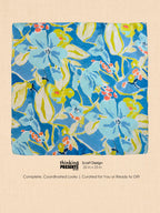 A square scarf with a vibrant floral pattern in blue, yellow, and coral pink, presented on a textured beige background with descriptive text below.