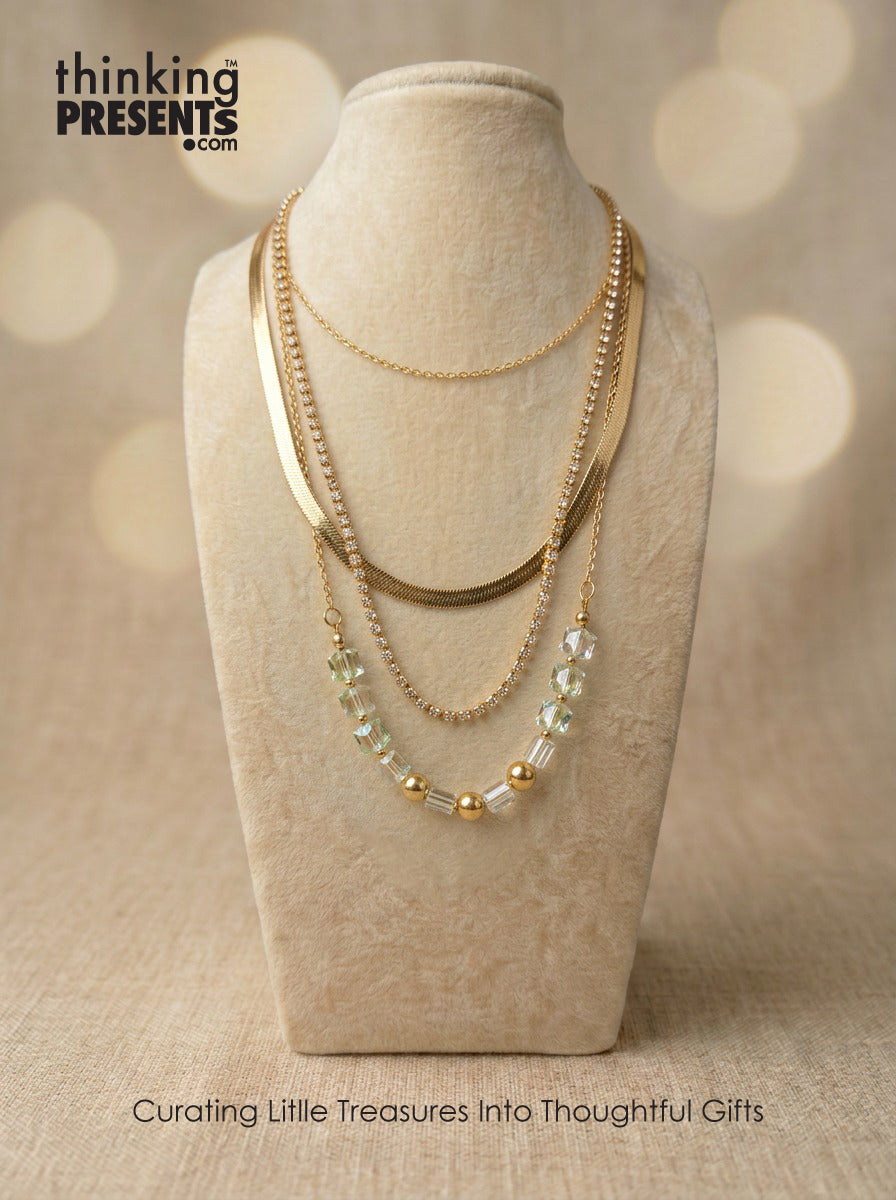 Layered gold-tone necklace with mixed chains and faceted green crystal accents, displayed on a neutral bust, part of the Green Reverie Gift Set by Thinking Presents™