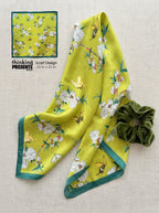 Yellow floral scarf with green trim and a matching scrunchie on a light background
