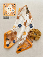 Scarf with floral pattern and scrunchie on a textured surface, featuring 'thinking presents' branding.