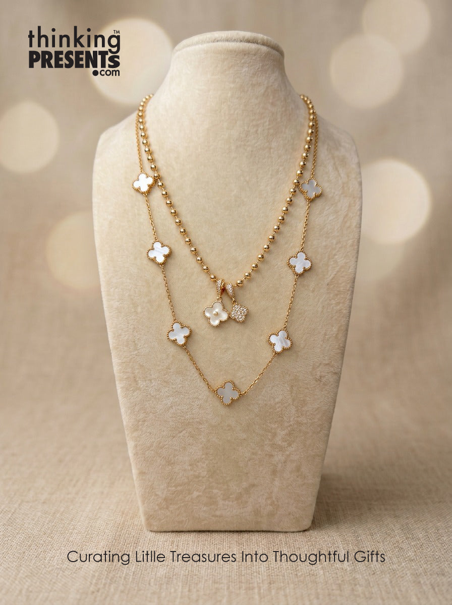 Gold necklace with floral pendants on a beige stand, with 'thinking PRESENTS' branding.