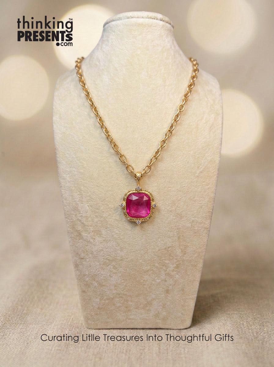 Gold-tone chain necklace with faceted magenta stone pendant and delicate crystal accents, styled on a neutral display, bold and feminine curated gift aesthetic