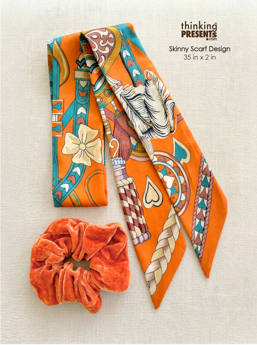Orange printed skinny scarf with turquoise and cream accents paired with a matching orange velvet scrunchie on a neutral fabric background.