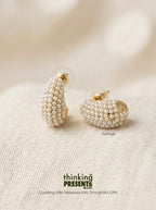Pearl bead cluster earrings with gold-tone posts, displayed on a textured beige fabric background. The brand name 'thinking PRESENTS' is visible at the bottom of the image.