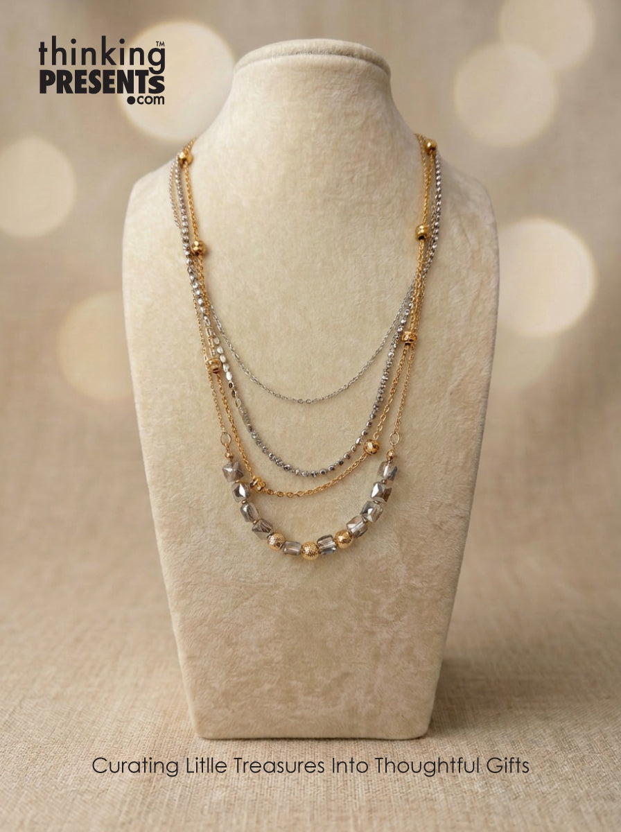 Layered gold and silver tone necklace with geometric bead accents displayed on a neutral fabric stand