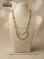 Layered gold and silver tone necklace with geometric bead accents displayed on a neutral fabric stand