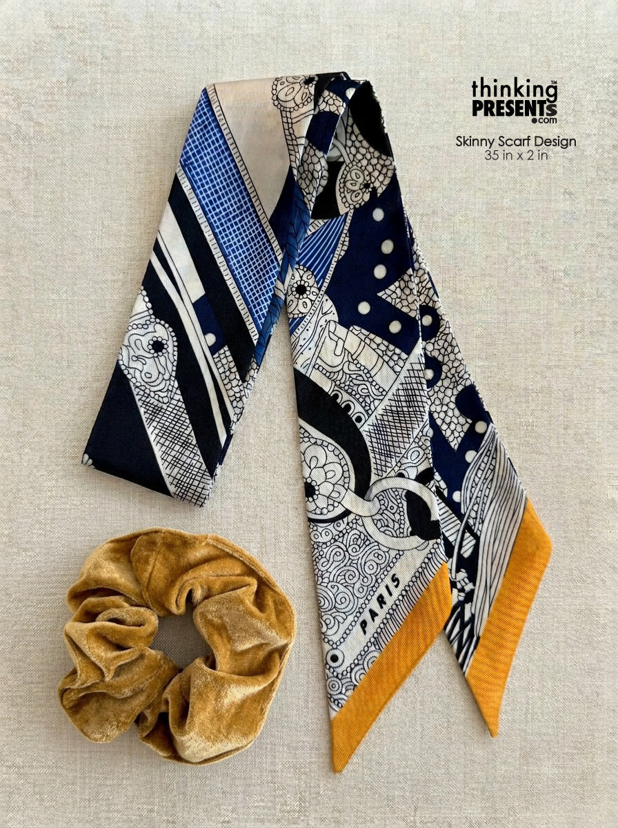 Navy blue and white patterned scarf with mustard yellow accents and a gold scrunchie on a light gray background.