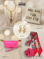 Curated gift set featuring layered gold-tone necklace with pink stone pendant and feather charm, matching hoop earrings with bow detail, five-piece ring set with mixed designs, bright pink wristlet pouch, and patterned red skinny scarf with matching scrunchie, styled as a bold and feminine ready-to-gift set