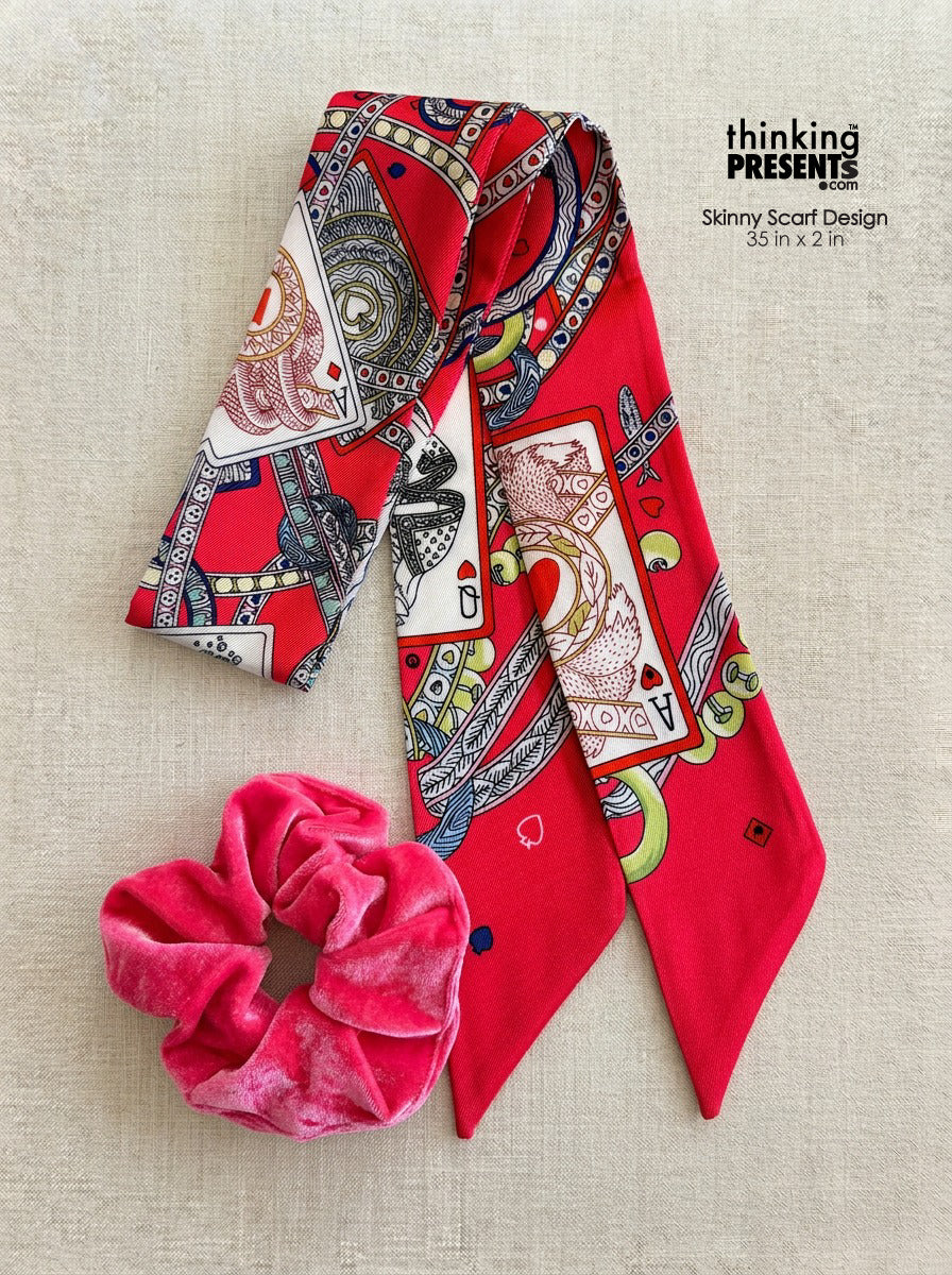Vibrant red patterned skinny scarf with playing card and chain motifs, paired with a soft pink velvet scrunchie, styled as part of a bold and playful curated gift set by Thinking Presents™