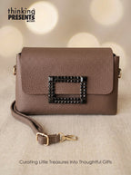 Brown handbag with decorative clasp on a beige background, featuring 'thinking presents' branding.
