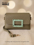 Green handbag with decorative clasp on a beige background, featuring 'thinking Presents' branding.