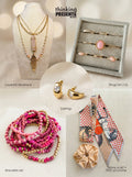 Curated gift set featuring layered gold-tone necklace with pink stone pendant, matching hoop earrings with heart detail, twelve-piece ring set with blush stones, stackable pink beaded bracelets, and a patterned skinny scarf with scrunchie, styled as a feminine ready-to-gift set