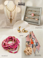 Curated gift set featuring layered gold-tone necklace with pink stone pendant, matching hoop earrings with heart detail, twelve-piece ring set with blush stones, stackable pink beaded bracelets, and a patterned skinny scarf with scrunchie, styled as a feminine ready-to-gift set