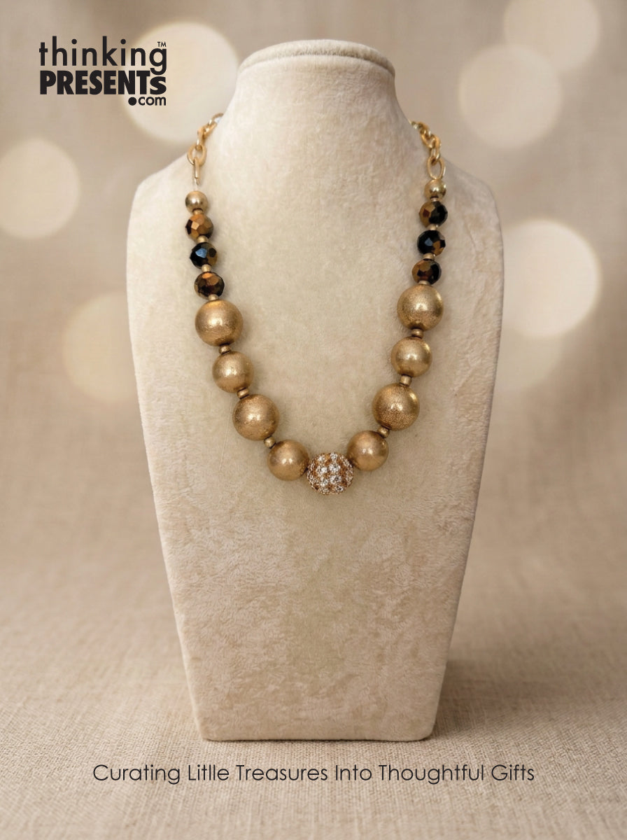 Gold beaded statement necklace with matte spheres, faceted accents and pavé center bead displayed on jewelry bust