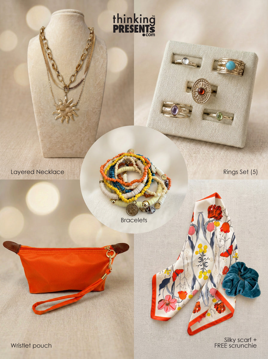 Curated gift set featuring layered gold-tone necklace with sun pendant, five-piece ring set with colorful stones, stackable beaded bracelets, vibrant orange wristlet pouch, and floral silky scarf with teal scrunchie, styled as a bold and playful ready-to-gift set