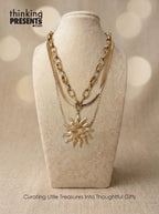 Gold necklace with a sun pendant on a beige stand, with 'thinking PRESENTS' branding.
