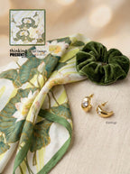 Scarf with floral design, green scrunchie, and gold earrings on a beige background