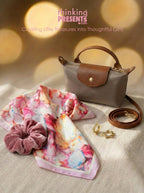 Small handbag, floral scarf, pink scrunchie, and gold earrings on a textured surface with 'thinking present' branding.