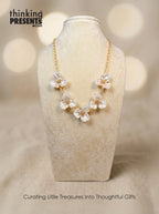 Gold-tone statement necklace with translucent white floral petals and crystal centers, displayed on a neutral jewelry stand, elegant and feminine style, Thinking Presents™ curated gift aesthetic