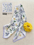 Silky floral scarf with soft lavender trim and delicate blue and yellow flowers, paired with a plush yellow scrunchie, styled as part of a feminine curated gift set by Thinking Presents™